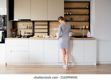 Young Woman With Beautiful Body Standing Next To A Modern Kitchen While Cooking. Back View