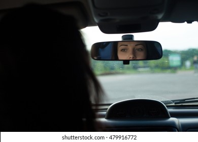 Young Woman With Beautiful Eyes Is Looking In Rearview Mirror In A Black Car.