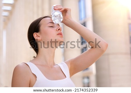 young woman, beautiful girl is suffering from Summer heat stroke, hot weather, sweaty and thirsty, refreshing with hand in blowing, holding cold water plastic bottle of water, high temperature 