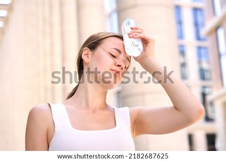 young woman, beautiful girl is suffering from Summer heat stroke, hot weather, sweaty and thirsty, refreshing with hand in blowing, holding cold water plastic bottle of water, high temperature