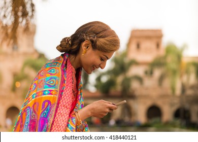 Young woman in beautiful park setting looking at her phone, smiling and texting