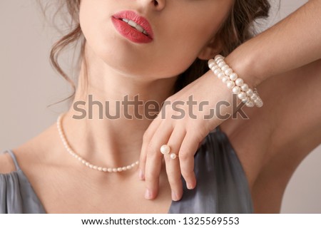 Young woman with beautiful pearl jewelry on light background, closeup