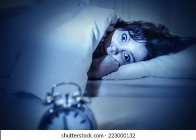 young woman in bed with alarm clock and eyes opened suffering insomnia and sleep disorder thinking about his problem on dark studio lighting in sleeping and nightmare issues - Shutterstock ID 223000132