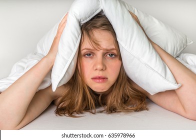 Young Woman In Bed Covering Ears With Pillow Because Of Noise