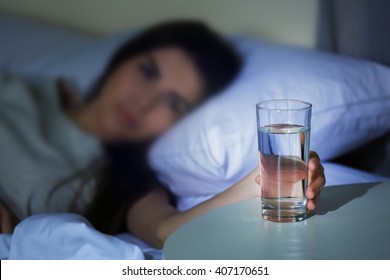 Young Woman In Bed Taking Glass Of Water From Table At Night