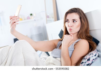 Young Woman In Bed Taking Selfie Making Duck Face