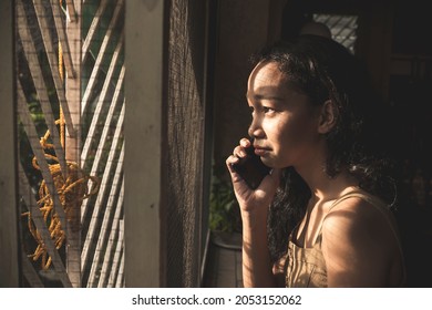 A young woman begins to cry and be overcome with emotions while realizing the bad news told to her via the phone. - Shutterstock ID 2053152062