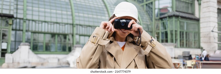 Young Woman In Beige Trench Coat And Baseball Cap Holding Vintage Camera, Banner