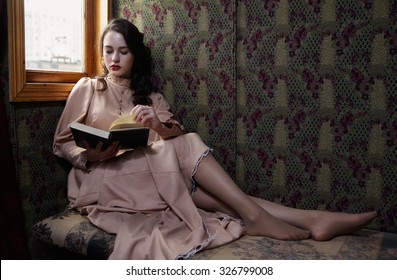 Young Woman In Beige Vintage Dress Of Early 20th Century Reading Book In Coupe Of Retro Railway Train