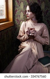 Young Woman In Beige Vintage Dress Of Early 20th Century Drinking Tea In Coupe Of Retro Railway Train