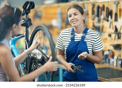 Young woman bicycle repair service worker in uniform advises female client - Powered by Shutterstock