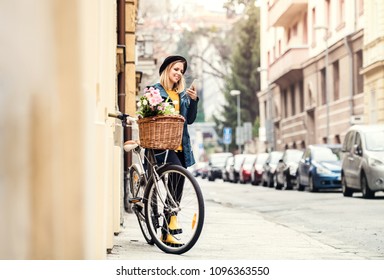 Young woman with bicycle and smartphone in sunny spring town.