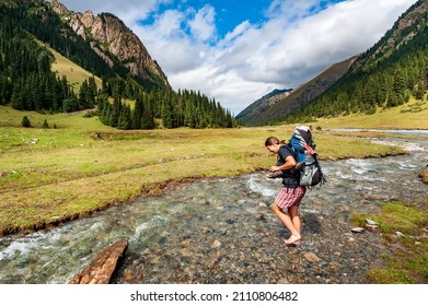 Young woman with big backpack barefoot crossing river. Shoeless female backapcker in river. Karakol valley, Issyk-kul region, Ala-kul lake Terskey Alatau mountain range, Kyrgyzstan, Central Asia. - Shutterstock ID 2110806482