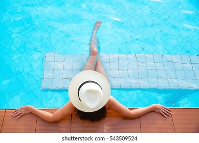 Young woman in big hat relaxing on the swimming pool 