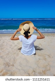 A Young Woman With A Big Hat Sitting On A Beach.