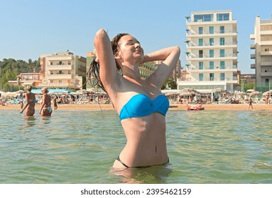 A young woman in a bikini adjusting wet hair on an urban beach - Powered by Shutterstock