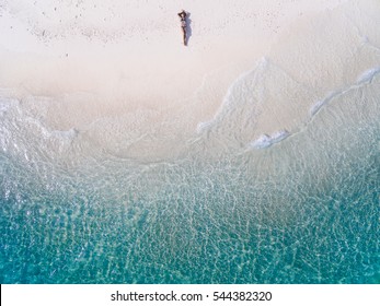 Young woman in a bikini lying on the back on the white sand near the waves of blue sea. Top view. Kai island, Andaman Sea, Phuket, Thailand. Aerial Shooting.