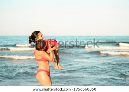 young woman in bikini plays with a child on the beach against the background of sea waves, laugh