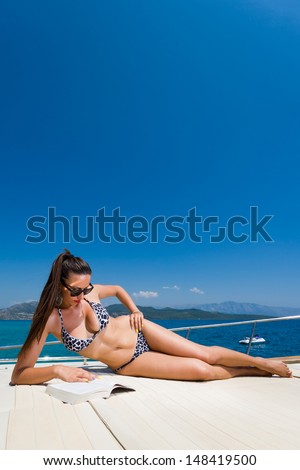 Young woman in bikini reading a book on her private yacht