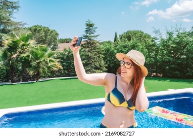 Young Woman In Bikini, Taking A Selfie At The Swimming Pool With Her Smartphone. Young Girl On Summer Holiday Sunbathing At Home. Concept Summer And Free Time.