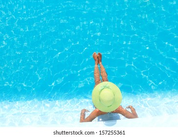 Young woman in bikini wearing a straw hat by the swimming pool