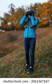 Young woman with binoculars watching birds in autumn park. Birdwatching hobby background image