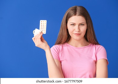 Young woman with birth control pills and condom on color background