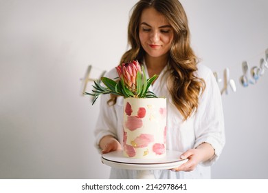 Young woman with birthday cake, close up. The cake is decorated with protea flowers. Holiday and confectionery concept