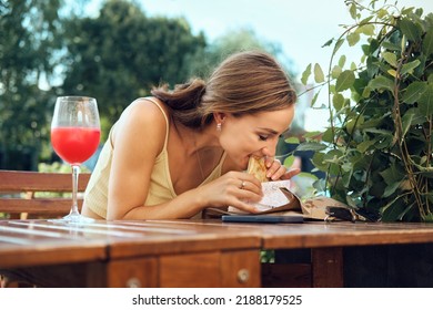 Young Woman Bites Slapjack Stuffed With Bacon, Ham And Cheese Sitting At Outdoor Terrace