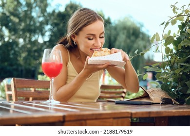 Young Woman Bites Thin Pancake Stuffed With Mushrooms, Ham And Cheese Sitting At Outdoor Terrace