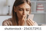 Young woman biting her nails while reading distressing news on her smartphone, feeling overwhelmed by the anxious message received, reflecting deep stress and concern in her expression