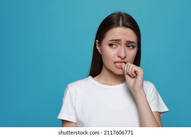 Young woman biting her nails on light blue background. Space for text - Shutterstock ID 2117606771