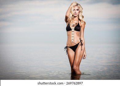 Young Woman In Black Bikini Posing In A Calm Sea While Sunset