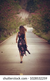 Young woman in black dress with flower pattern background walking on a country road in the forest in summer season. Photo toned style Instagram filters