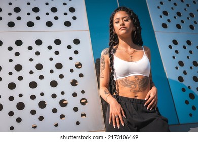 Young Woman Of Black Ethnicity With Long Braids And With Tattoos, In The City Enjoying The Sun