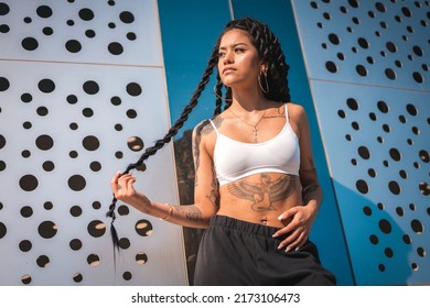 Young Woman Of Black Ethnicity With Long Braids And With Tattoos, In The City Enjoying The Sun