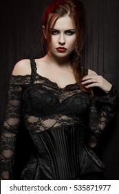 Young woman in black gothic costume on dark background