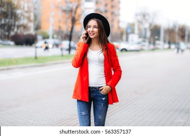 Young Woman In Black Hat Using Mobile Phone On City Street. Girl Talking On The Phone