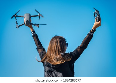 Young woman in black jacket holding remote control and drone before the flight on the blue sky background. Flying drone outside in summer.