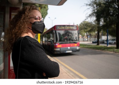 Young Woman With Black Mask Waiting For The Bus In The City. Prevention Of Covid 19 Or Coronavirus In Public Transport.