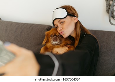 Young Woman In Black Pajamas And Bandage For Sleeping. Girl Photographs Herself With A Dog On The Phone. Grey Sofa.