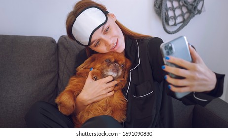 Young Woman In Black Pajamas And Bandage For Sleeping. Girl Photographs Herself With A Dog On The Phone. Grey Sofa.