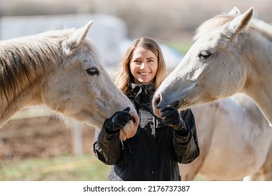 Young woman in black riding jacket standing near group of white Arabian horses smiling happy, one on each side, closeup detail - Powered by Shutterstock