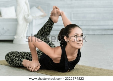 a young woman in black sportswear shows yoga asanas and does pilates