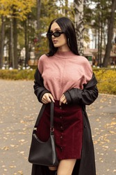 Young Woman In Black Sunglasses, Leather Raincoat, Pink Turtleneck And Red Skirt. Natural. Attractive Brunette Woman In Park. Youth Fashion