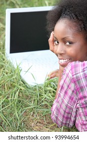 Young woman with a blank screened laptop in the grass