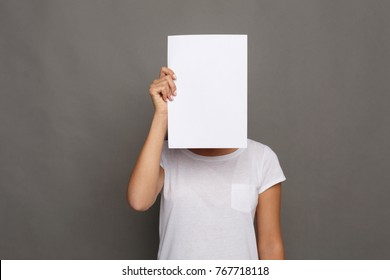 Young woman with blank white paper at face. Serious girl covering her head with advertising sheet, copy space - Powered by Shutterstock