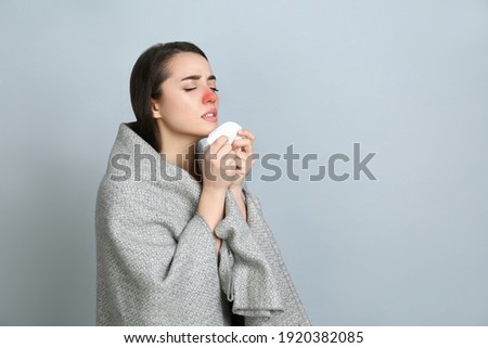 Young woman with blanket sneezing on light grey background, space for text. Runny nose