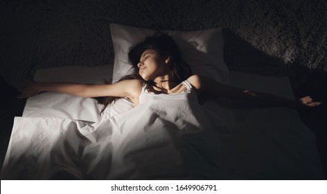 Young Woman Blissfully Sleeping In Bed Spreading Arms Wide, Sunbeam Falling On Her Face