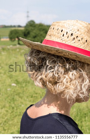 young woman with blond curls from behind with a straw hat in fro